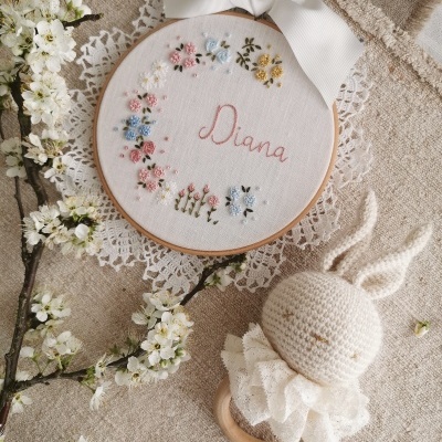 bastidor bordado com flores e nome Diana, laço branco, brinquedo coelho de crochê e flores brancas