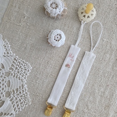 Prendedores de mala para bebé em tecido branco com clipes dourados e rendas sobre tecido bege