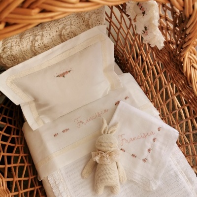 Conjunto de bebé branco bordado com nome Francisca e brinquedo de crochê em poltrona de vime