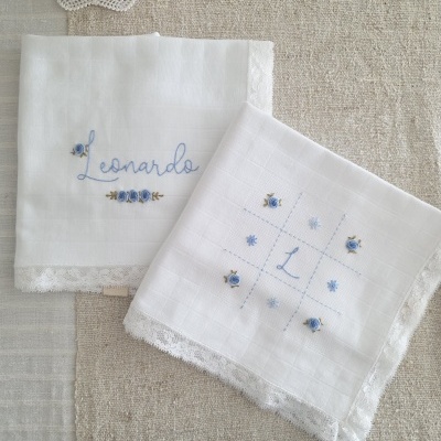 Dois lenços brancos bordados com nome e letra, decoração de flores azuis e acabamento em renda