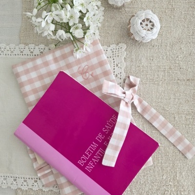 Caderno rosa em pano xadrez rosa com flores brancas e ornamentos de crochê sobre tecido bege