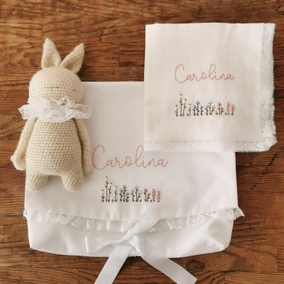 Boneca de croché e dois tecidos brancos bordados com o nome Carolina e flores sobre uma superfície de madeira
