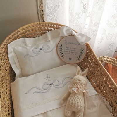 Berço de vime com roupa branca bordada azul, coelho de tricô e moldura bordada com nome.