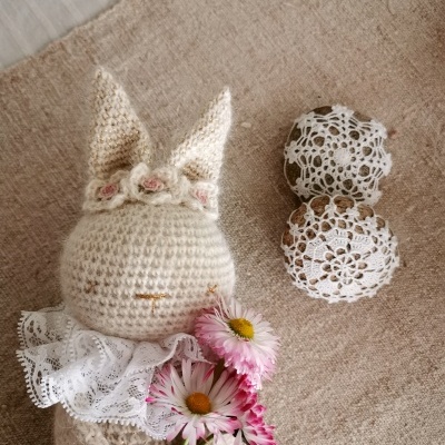 Boneco de croché com renda, flores e objetos com renda sobre tecido bege