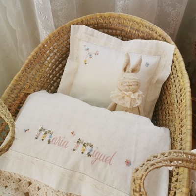 Berço de verga com almofada e manta branca bordada, boneco de croché coelho, cortinas brancas ao fundo