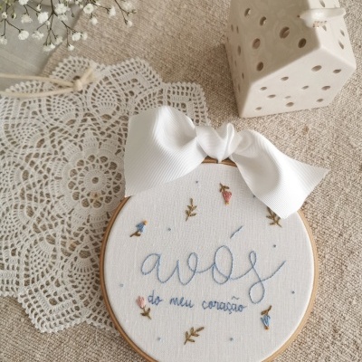 Quadro bordado com frase e flores, fita branca, em ambiente rústico com toalha de renda e vela branca