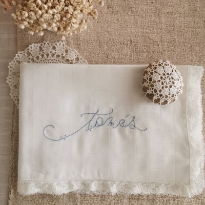 Toalha branca bordada com nome Tomás e borda rendada sobre tecido e decoração seca