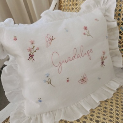 Almofada branca com bordados de flores, borboletas e o nome Guadalupe em cadeira de verga