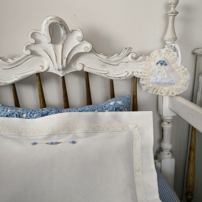 Cama branca de madeira antiga com fronhas bordadas e almofada azul floral