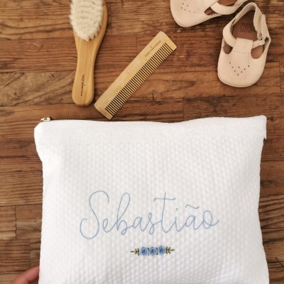Necessaire branca bordada com nome, escova, pente e sapatos de bebé sobre madeira