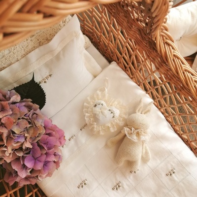 Travesseiro branco com bordados delicados e bonecos de tecido sobre almofada de vime