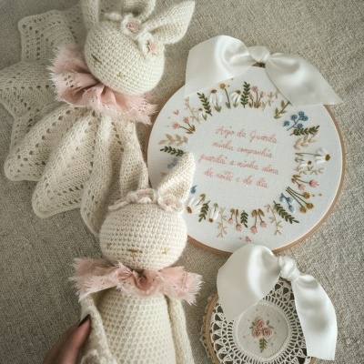Bonecos de coelho em crochet com cachecóis cor de rosa e bordados florais com texto em bastidor