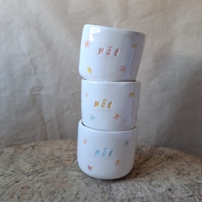 Três chávenas brancas empilhadas com a palavra mãe e desenhos florais coloridos.