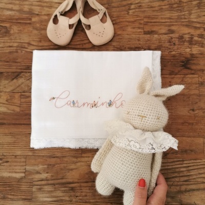 Sapatos de bebé, fralda bordada e boneco de crochê sobre madeira