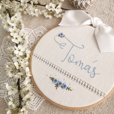 Bastidor bordado com nome Tomás e flores azuis junto a flores brancas e renda