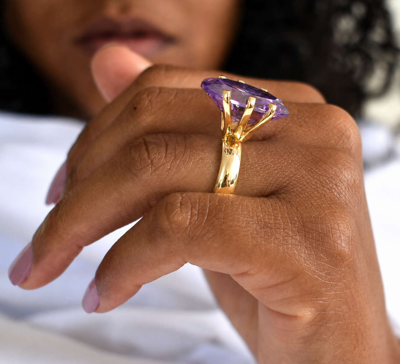 Anel Tribus Anel dourado com pedra roxa num dedo de pele castanha