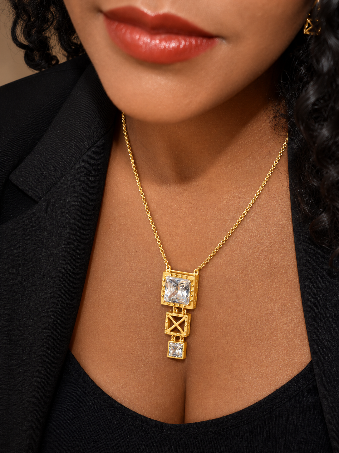 Colar Ponte 3 Colar dourado com pendentes quadrados e pedras transparentes no pescoço de pessoa com blusa preta