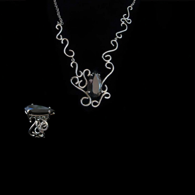 Conjunto de colar e anel em prata com pedra preta em fundo preto.