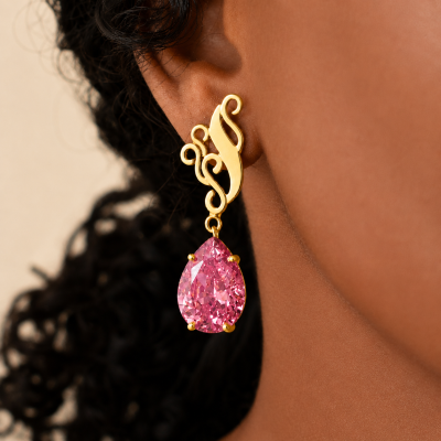 Brinco dourado com pedra rosa em formato de gota na orelha.