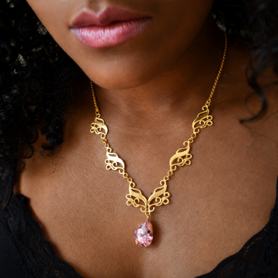 Colar dourado com pendente de pedra rosa em gota no pescoço de mulher.