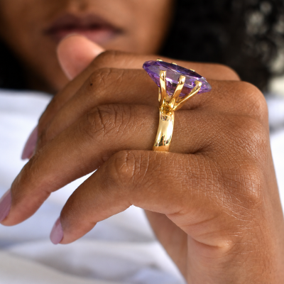 Anel dourado com pedra roxa num dedo de pele castanha