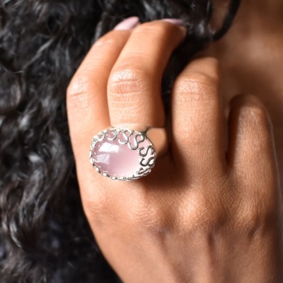 Anel prateado com pedra rosa oval e borda decorativa na mão