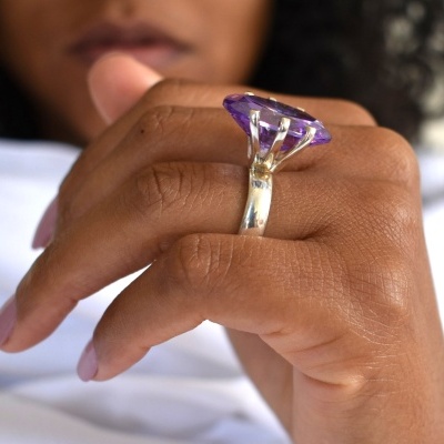 Anel prateado com pedra violeta facetada no dedo médio