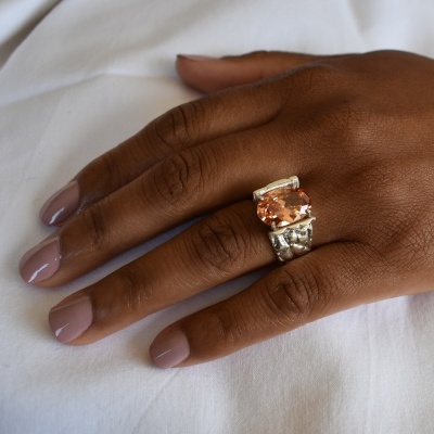 Anel com pedra cor de pêssego em mão feminina com unhas pintadas rosa claro