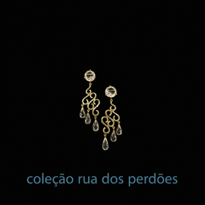 Brincos dourados com pedras transparentes e gotas, texto coleção rua dos perdões.