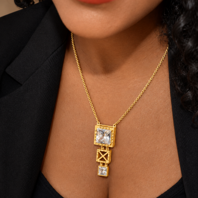 Colar dourado com pendentes quadrados e pedras transparentes no pescoço de pessoa com blusa preta