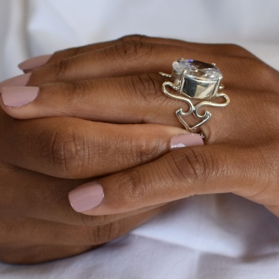 Anel prateado com pedra transparente em mão com unhas rosa claro