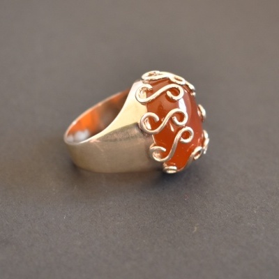 Anel com pedra oval laranja e ornamentos metálicos.