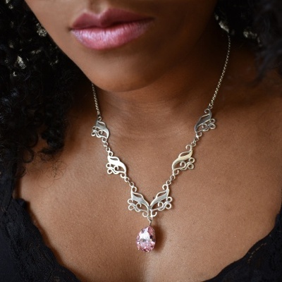 Colar prateado com pendente em pedra rosa em forma de gota usado no pescoço