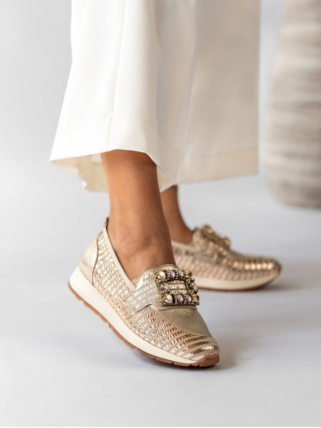 Mocassim MLV Alicia.20 Gold Sapatos ténis dourados com fivela decorativa e calças brancas.