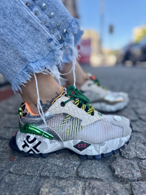 Sapatilhas ExéK134White Tênis desportivo colorido com padrão texturizado e calças de ganga azuis desfiadas em chão de pedra