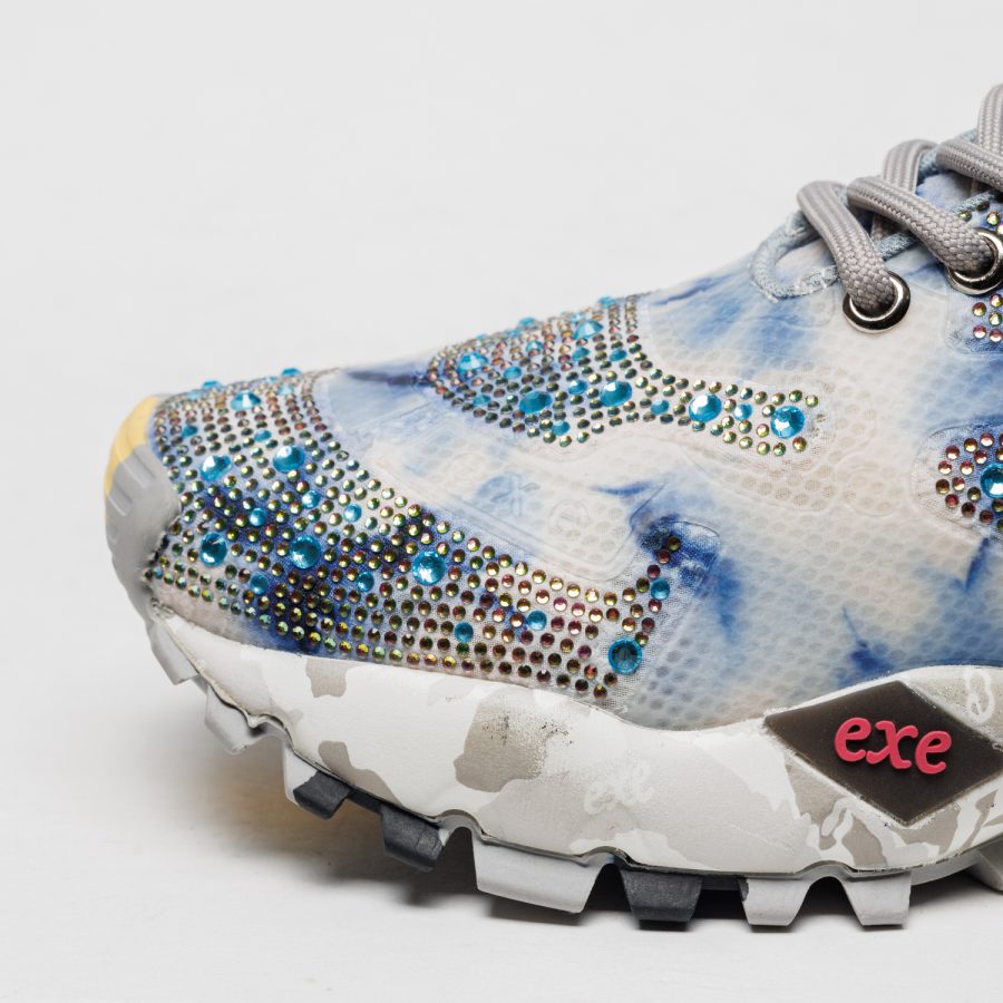 Sapatilhas Exé 134-20 Grey White Parte frontal azul clara e branca de ténis com strass azuis e etiqueta exe rosa.