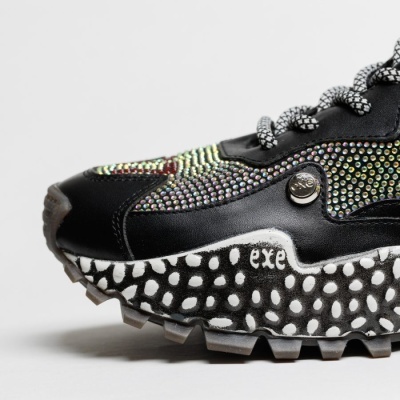 Ténis pretos com detalhes iridescentes e sola padrão bolinhas com texto 'exe'