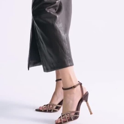 Sandálias de salto alto castanhas com tiras entrelaçadas e saia preta comprida com fenda.