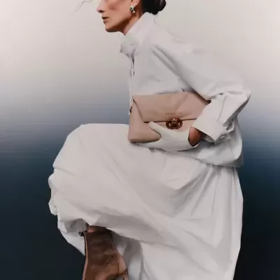 Mulher vestida de branco com botas castanhas e bolsa bege com fecho metálico