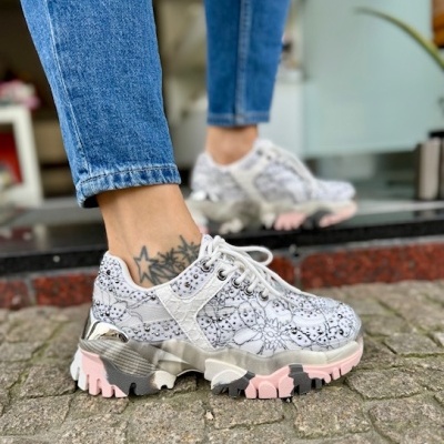 Ténis brancos florais com sola rosa e preta usados por pessoa com calças de ganga