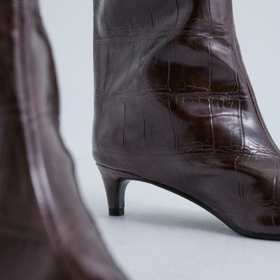 Botas castanhas de salto médio com textura de pele de crocodilo em fundo branco