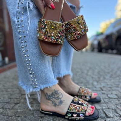Sandálias decoradas com miçangas coloridas em castanho e preto sobre pavimento de pedra