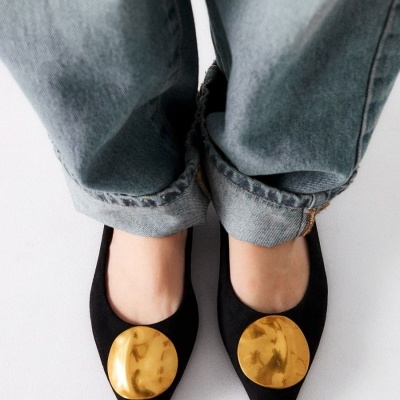 Sapatos rasos pretos com detalhe dourado usados com jeans azuis claros enrolados