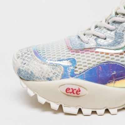 Ténis desportivo branco com detalhe em tecido felpudo cinzento, aplicações metálicas iridescentes e sola branca com logótipo exè vermelho