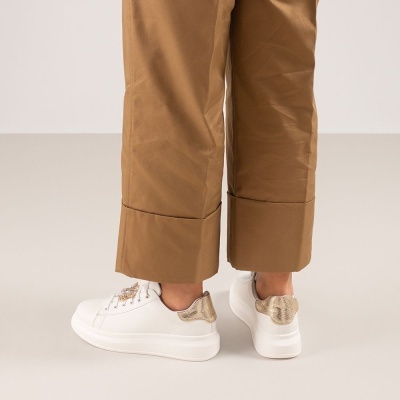 Ténis brancos com padrão pele de cobra usados com calças castanhas