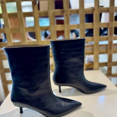 Botas pretas de salto fino com textura imitando pele de crocodilo em mesa branca