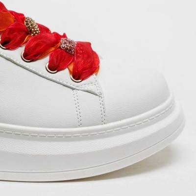 Ténis branco com atilhos de tecido vermelho e laranja e brilhantes.