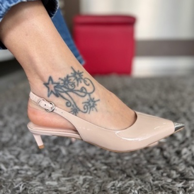Sapato slingback bege claro com salto médio usado num pé com tatuagem preta