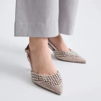 Sapatos de salto baixo bege com pedras brilhantes e calças cinza.