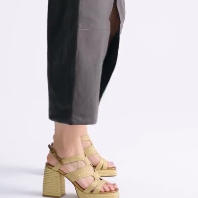 Mulher a usar sandálias de salto alto bege e vestido preto longo com fenda.